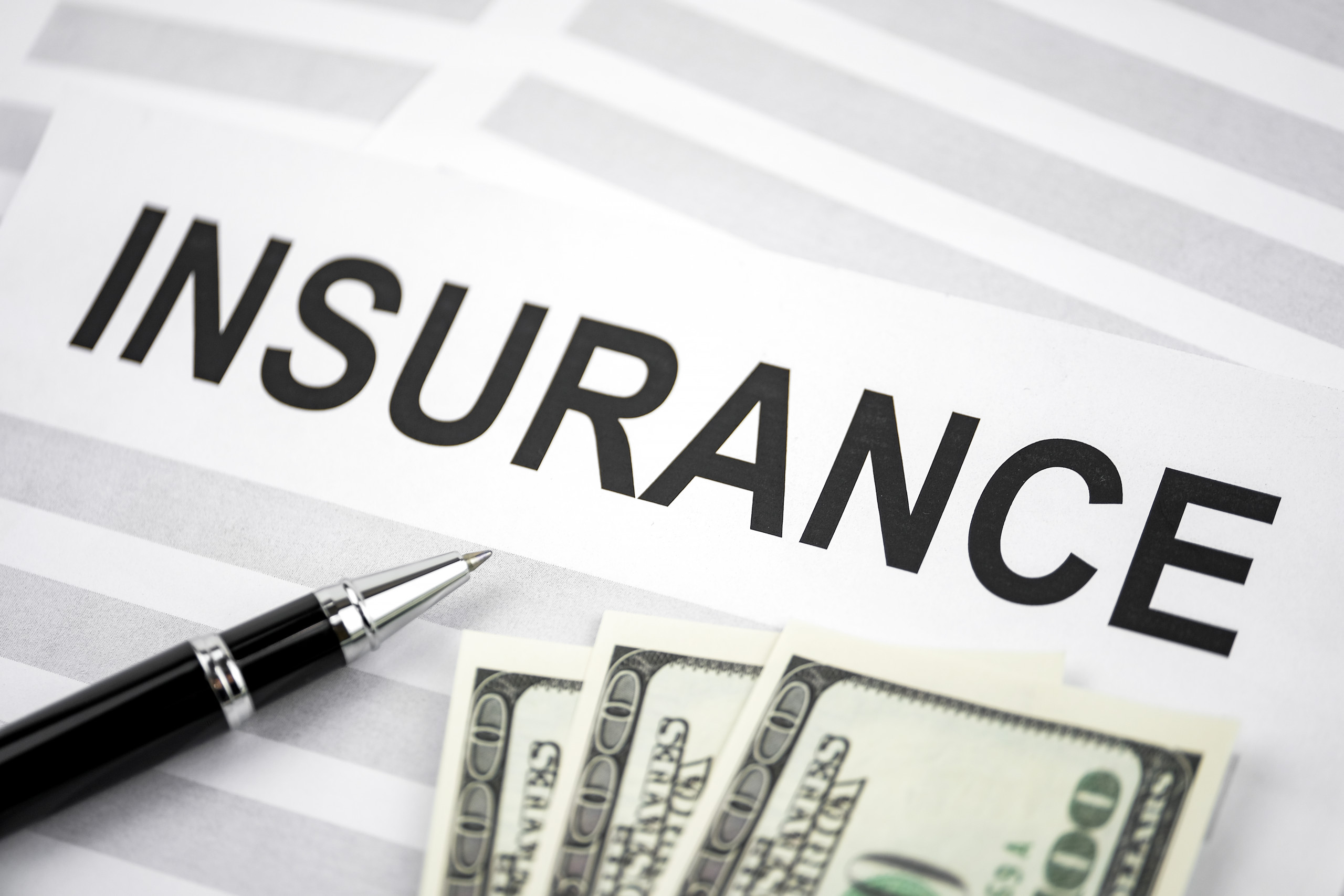Concept of expensive insurance. Pen lying with paper printed out the word "insurance" and US dollar bills.